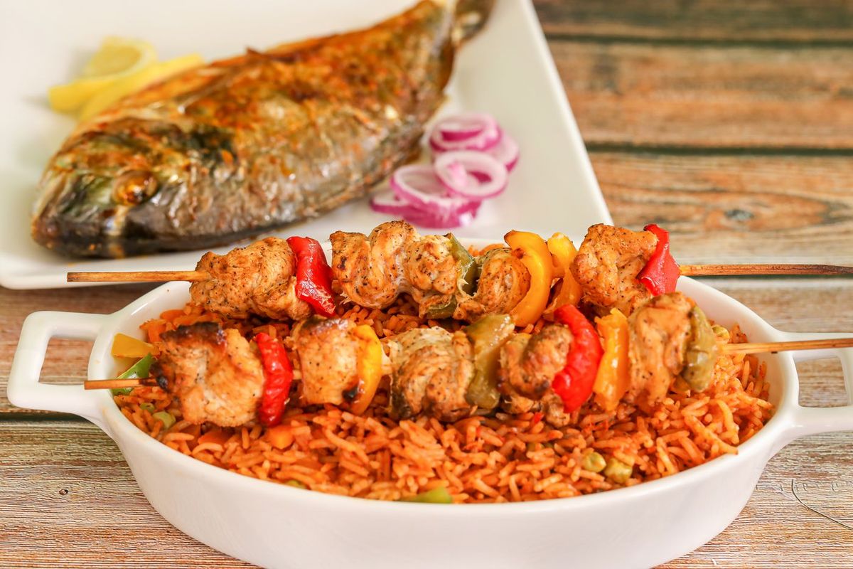 A dish of jollof rice with chicken skewers and grilled fish