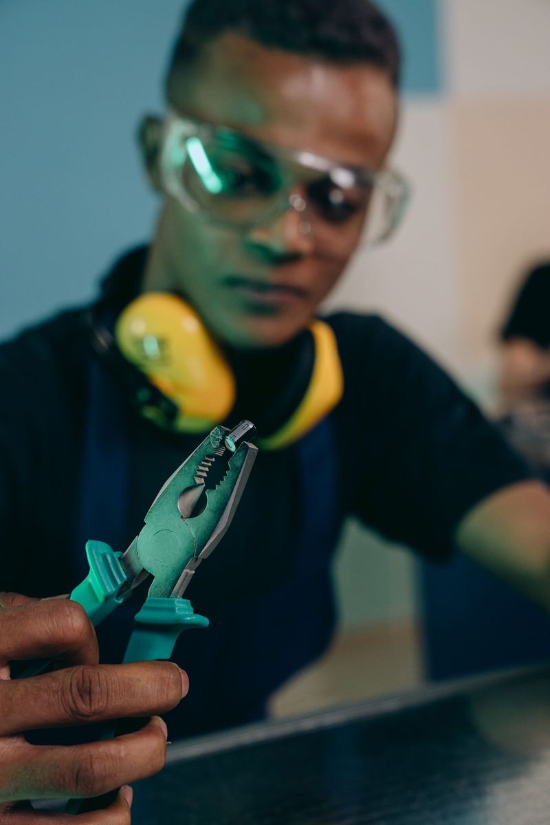 A tradesman in safety glasses and ear defenders holding a pair of pliers